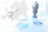A man dressed in a business suit stands in front of a European map, meticulously studying a business graph.