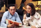 An intellectual duo engrossed in a book, engaged in a discussion at a table.