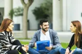 Three students sitting on the grass engaged in conversation.